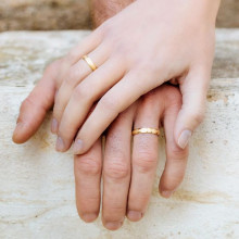 Manos con alianza de boda de oro amarillo con bordes pulidos y matizado arena con diamante
