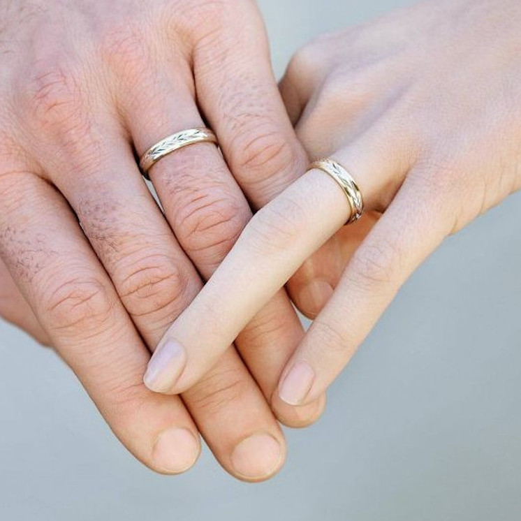 Manos con alianzas de boda con dibujo de espiga en oro de dos colores