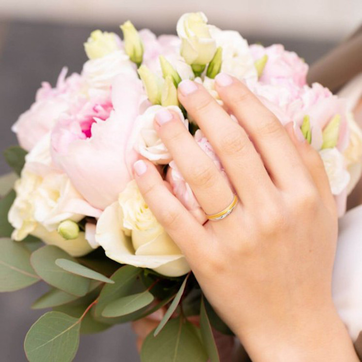 Mano en ramo de novia con alianza bicolor con diamante