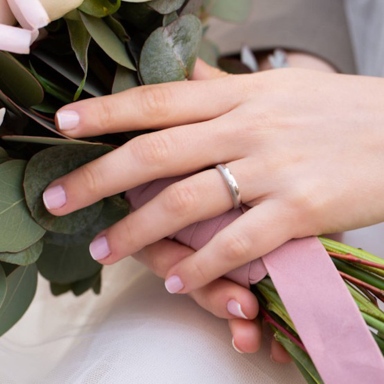 Manos en ramo de novia con alianza de oro blanco y diamante