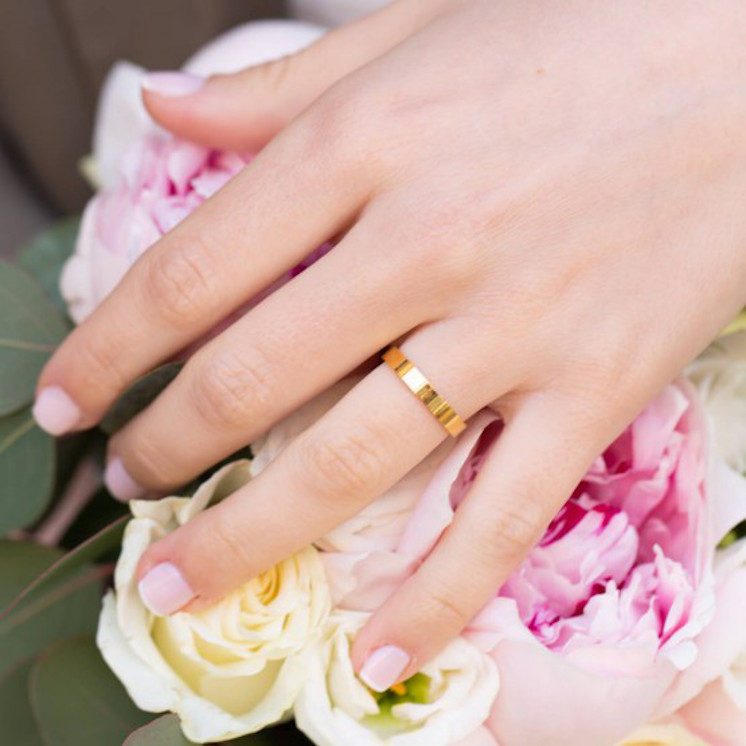 Mano en ramo de novia con alianza plana de oro amarillo